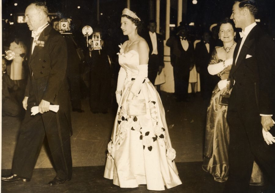 Queen Elizabeth attends a ball dressed in a formal gown. Cameramen snap her photo.