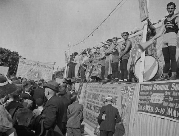 Black and white photograph of boxers standing on a platform in front of a large crowd.