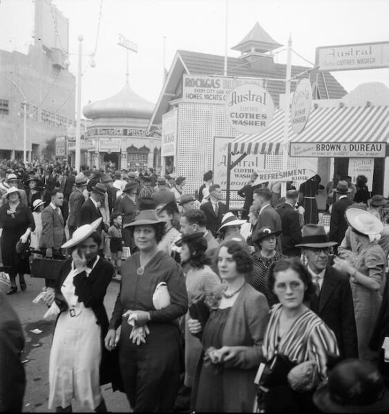 A scene from the Royal Agricultural Show. In the foreground are women. In the background is a crowd of people. A refreshment kiosk is noticeable in the background.