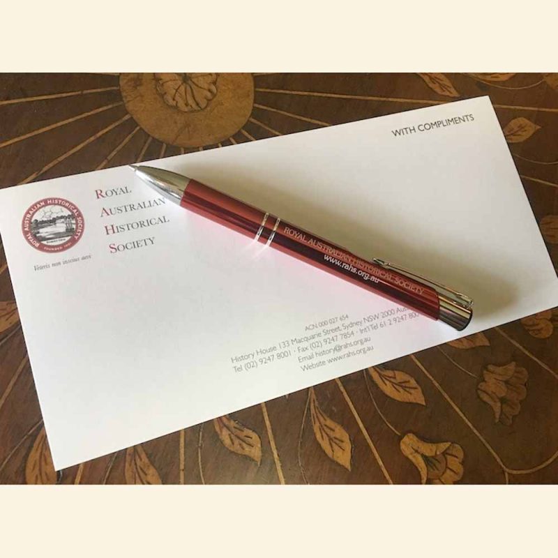 Royal Australian Historical Society writing pen which has a metallic red and silver shaft colour and is resting on top of an envelope