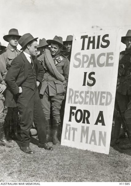 Australian soldiers on a recruitment drive encourage a man to enlist. The poster reads: THIS SPACE IS RESERVED FOR A FIT MAN.