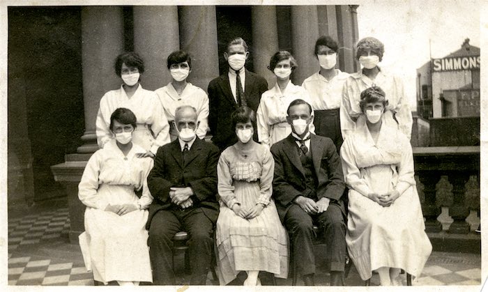A group of men and women wearing white medical masks have their photograph taken at Town Hall.
