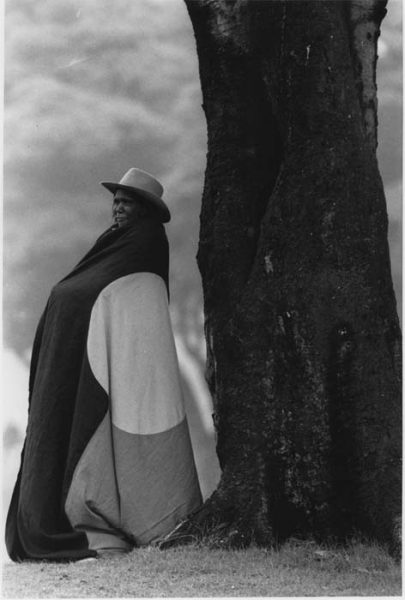 A black adn white photograph of Essie Coffey wearing the Aboriginal flag wrapped around her.