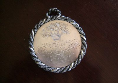 A silver medal engraved with the words 'Australian Foral and Horticultural Society'. A design of a bushel of fruits, vegetables and flowers in a basket is engraved at the top.