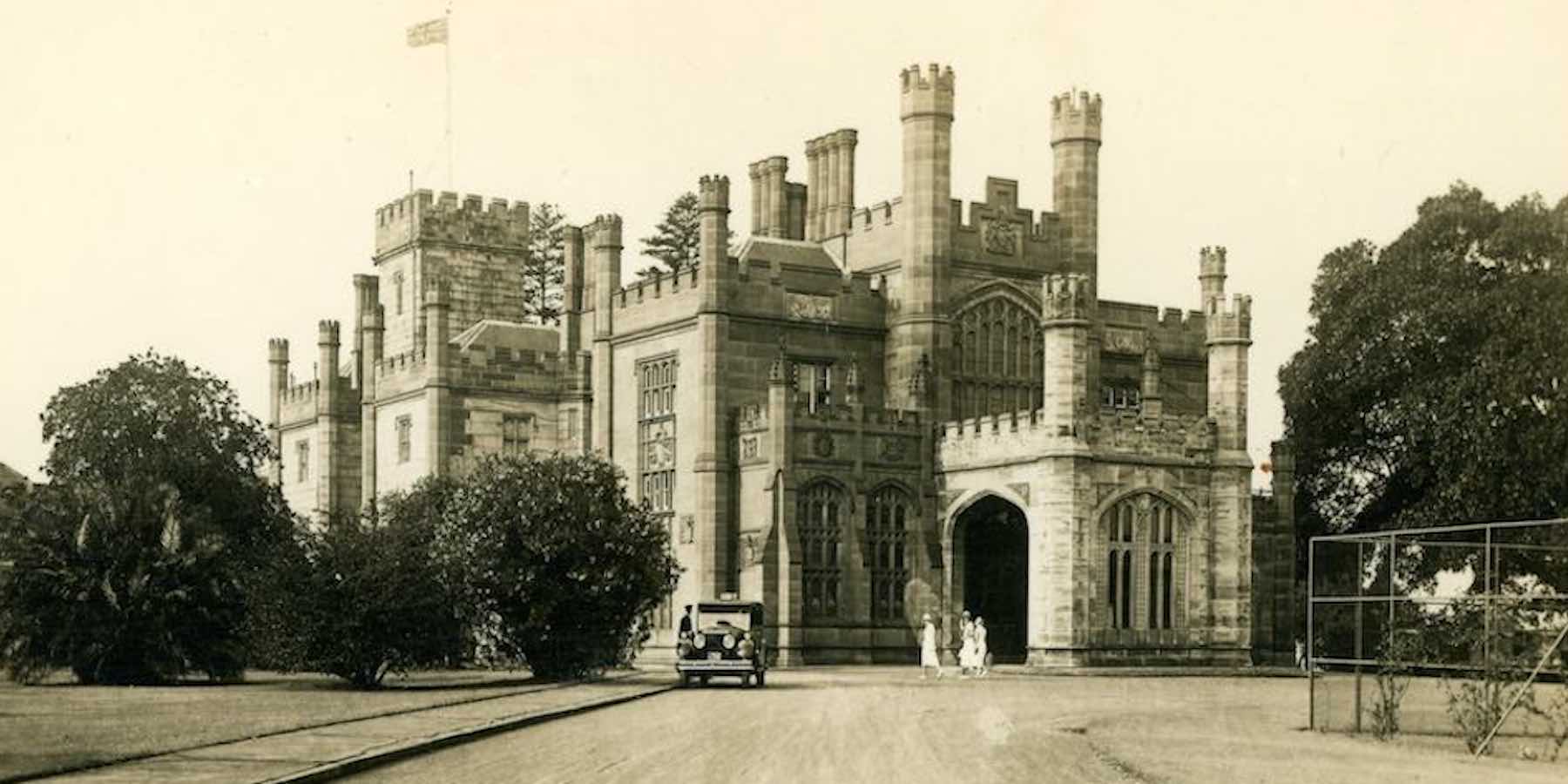 Sepia photograph of NSW Government House from the 1930s. A group of women dressed in white cloths walk towards a car being manned by a driver.