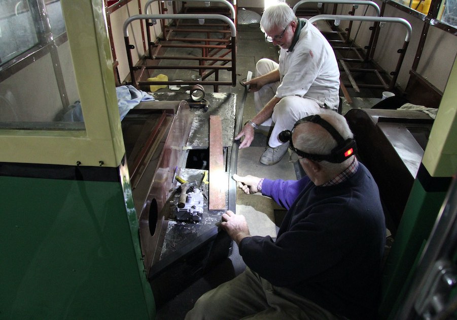 Two men work are reupholstering a seat on a heritage bus.