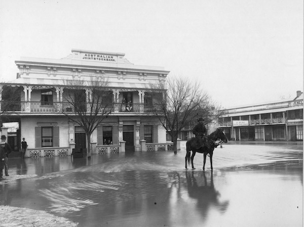 Black and white photograph of the Australian Joint Stock Bank in Wagga Wagga. The ground appears flooded, and a man sits on a horse.