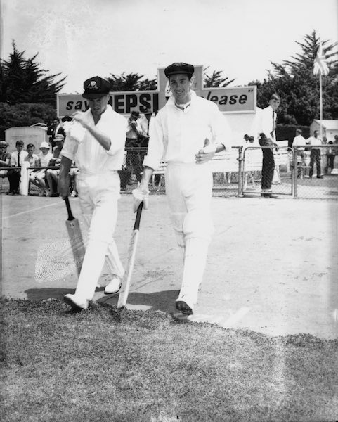 Photograph of two cricket players walking onto the pitch during a game.