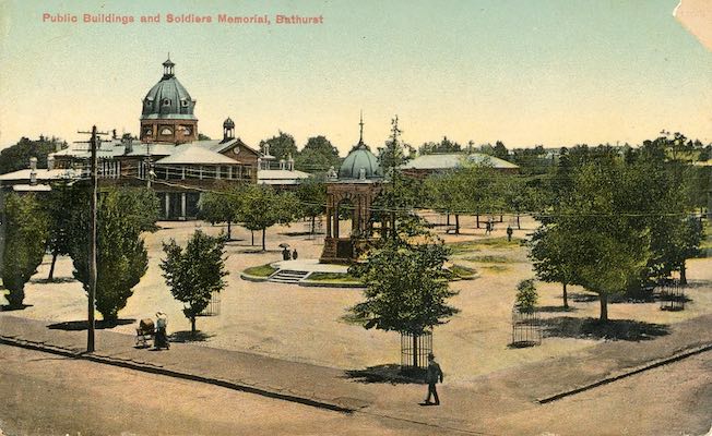 Postcard showing the Soldiers Memorial at Bathurst. The memorial is situated in the centre of a park lined with trees. A public building is visible in the background.