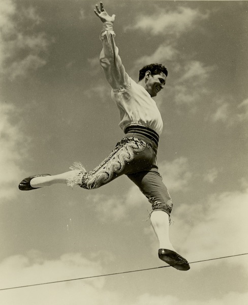 Con Colleano balances on a high wire on one foot. Con appears to be dressed in traditional Spanish attire.