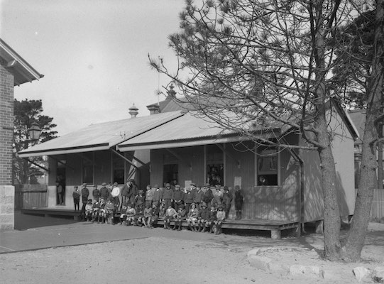 A portable classroom with students and teachers sitting on the verandah