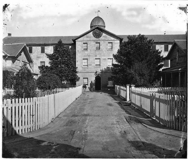 A glass negative showing a picket-fenced path leading to a sandstone building with a clock on its face.