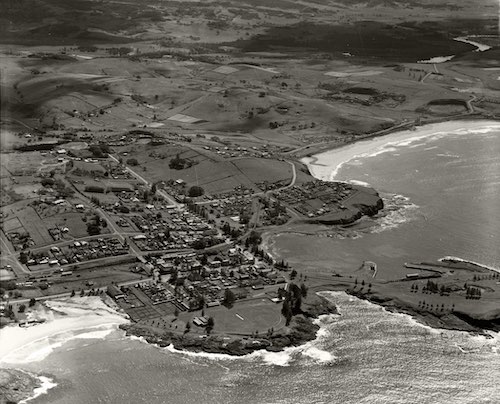 Aerial view of Kiama looking northwest. The foreground features Bombo Beach, Kiama ocean pool, Black Beach, Kiama harbour, Kiama Surf Beach, with a view of rural farmland in the background.
