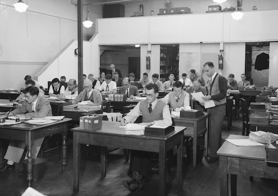 Neatly dressed male office workers at sitting at their desks filling in paperwork.