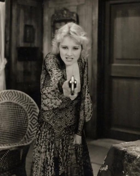 A woman angrily points a pistol at an unknown person off-screen