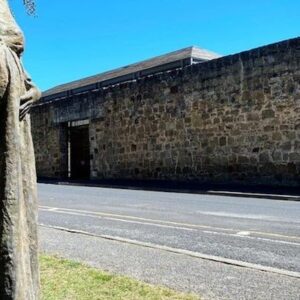 In the foreground is a statue of a visible pregnant female convict. The stone wall of the Cascades Female Factory is in the background.